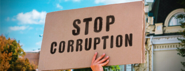 Man holds cardboad sign reading 'Stop Corruption.'